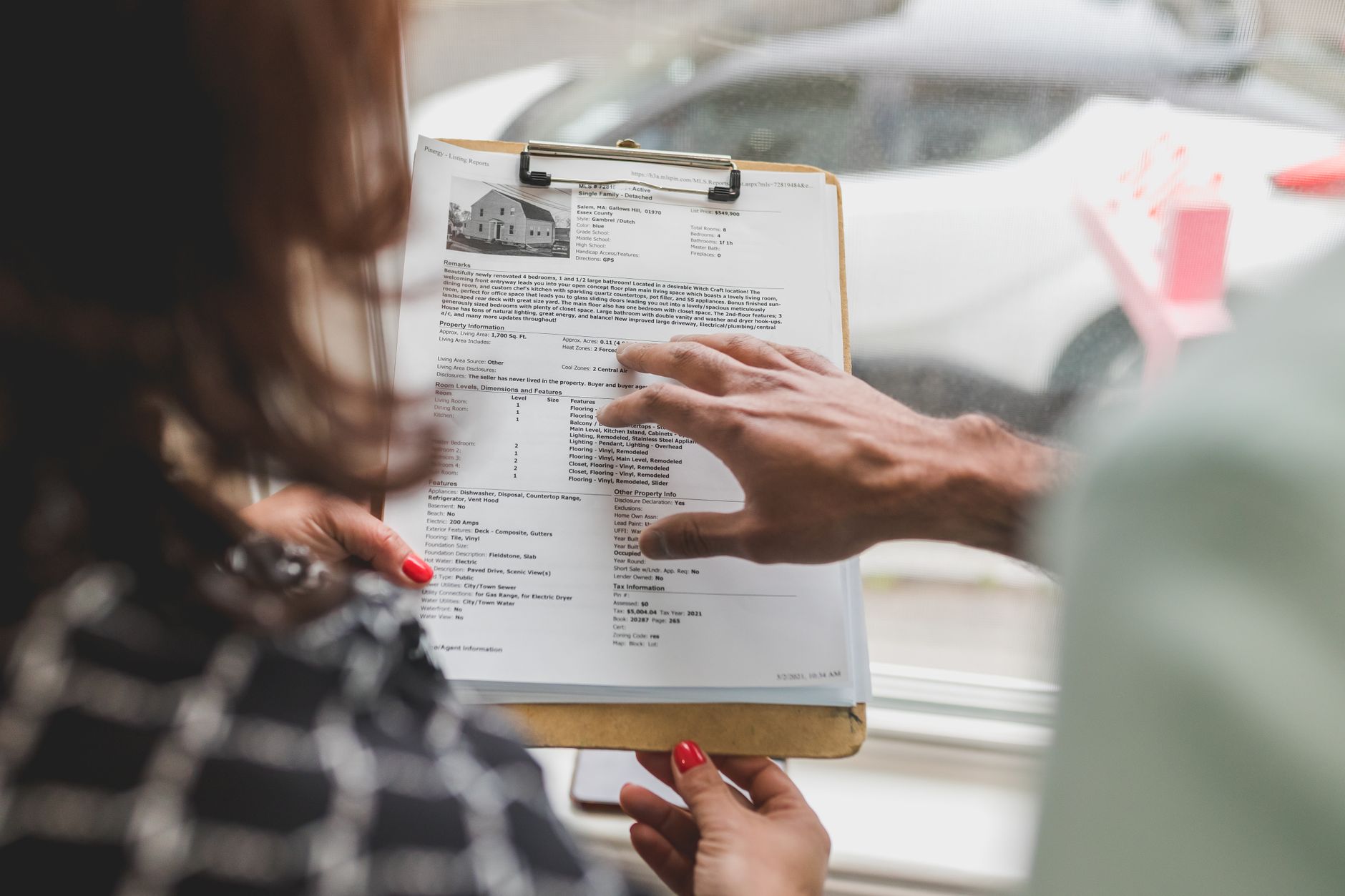 Close view of a printed property listing on a clipboard while a hand points to a line on the page.