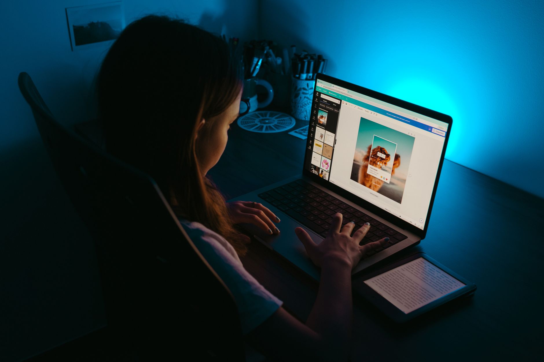 A girl uses a laptop at a desk in a dimly lit room lit by a calm blue light.
