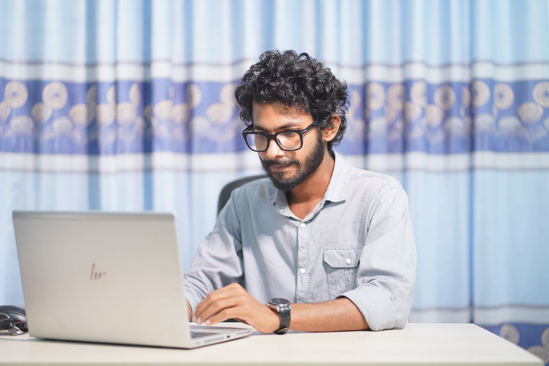 A focused young man using a laptop in a well-lit room at home.